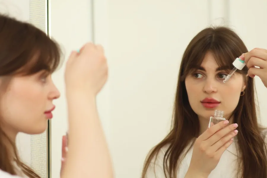 Person applying skincare serum in front of a mirror