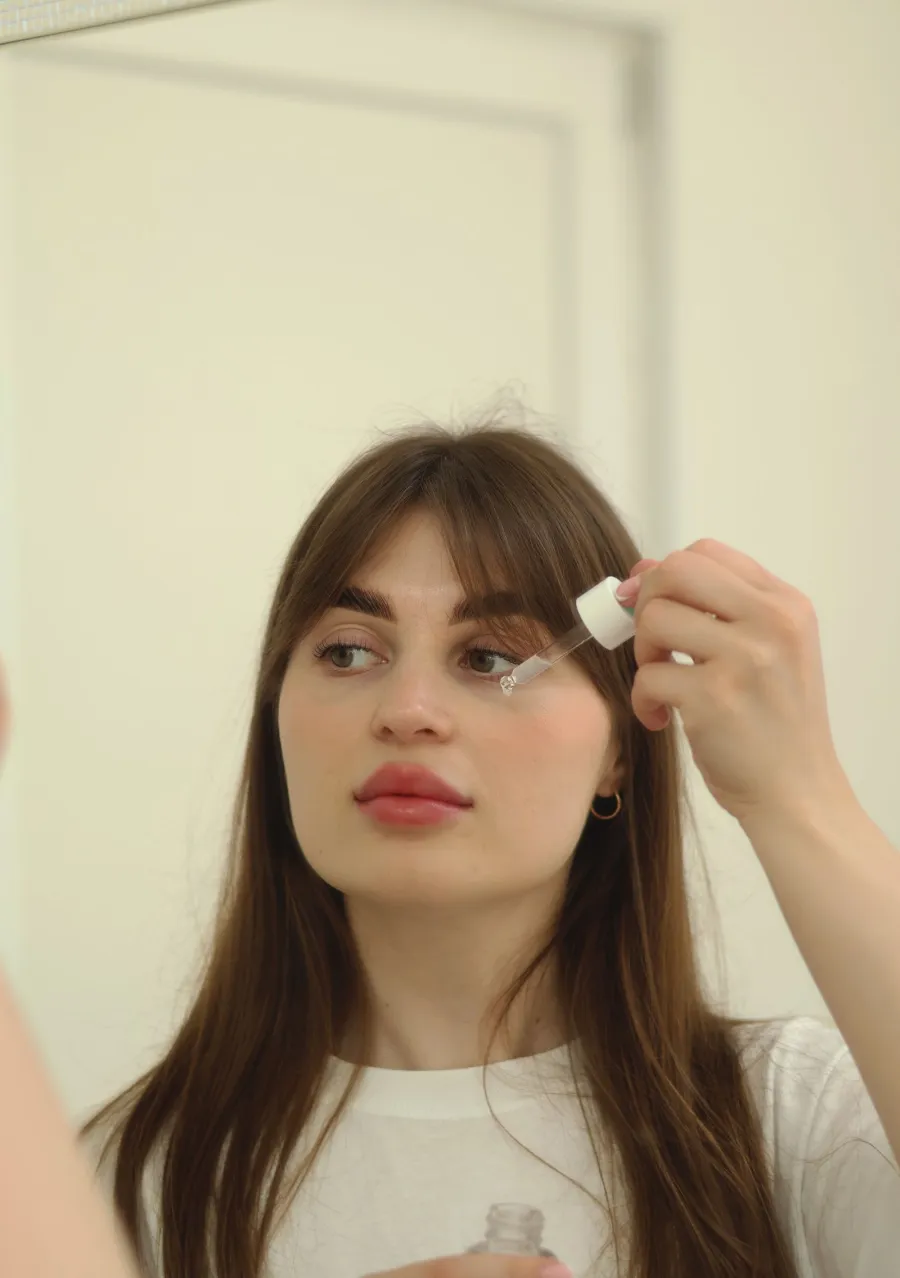 Person applying skincare with a dropper in front of a mirror