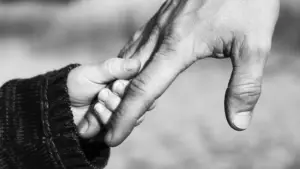 Child’s small hand gripping an adult’s finger in black-and-white.