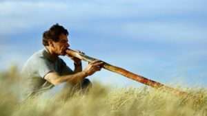 a man in the grass blowing a didgeridoo