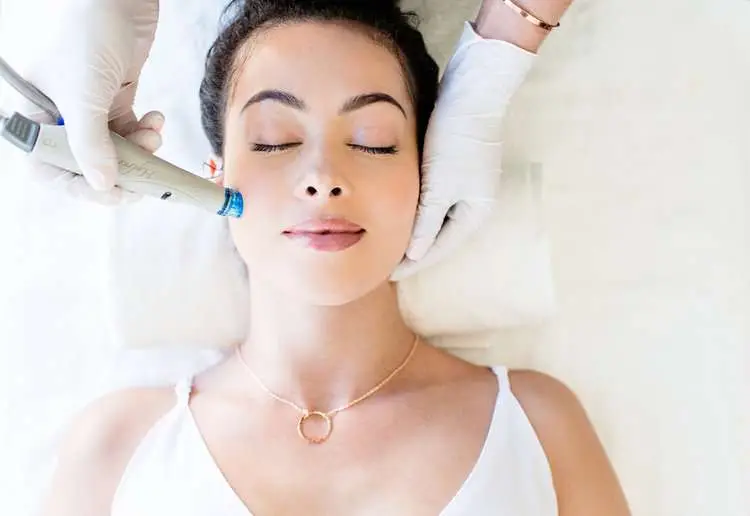 Woman receiving a Hydrafacial treatment, eyes closed, lying on spa table.