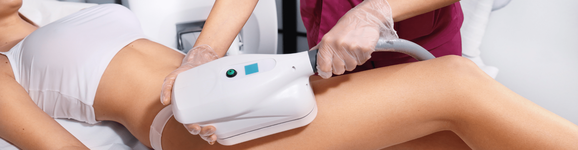 A professional in a clinical setting using a large handheld laser device to perform a cosmetic procedure on a client's thigh.