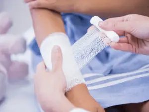 Medical professional's hands wrapping the bandage around the patient's wounded hand
