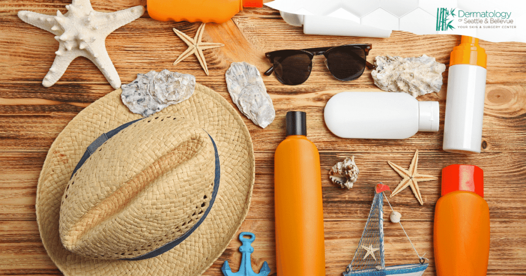 Flat lay of summer beach essentials including a straw hat, sunglasses, sunscreen bottles, seashells, starfish, and other beach accessories, with the Dermatology of Seattle & Bellevue logo in the corner.
