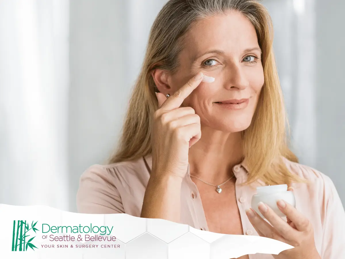 Smiling middle-aged woman applying moisturizer to her face, promoting skincare and wellness, associated with Dermatology of Seattle & Bellevue