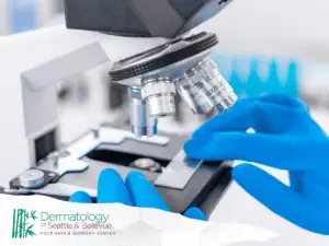 Gloved hands adjusting glass slide under microscope in laboratory.