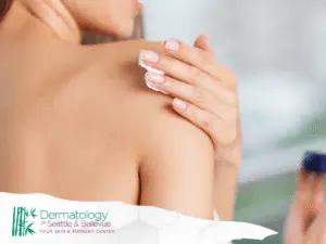Woman applying white cream to bare shoulder with manicured hand