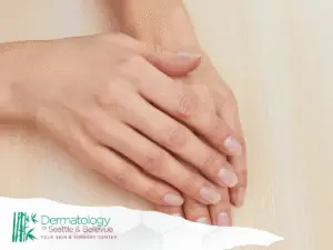 Close-up of crossed hands resting on light wooden surface.