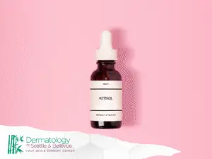 Brown dropper bottle labeled “retinol” on pink background with logo.