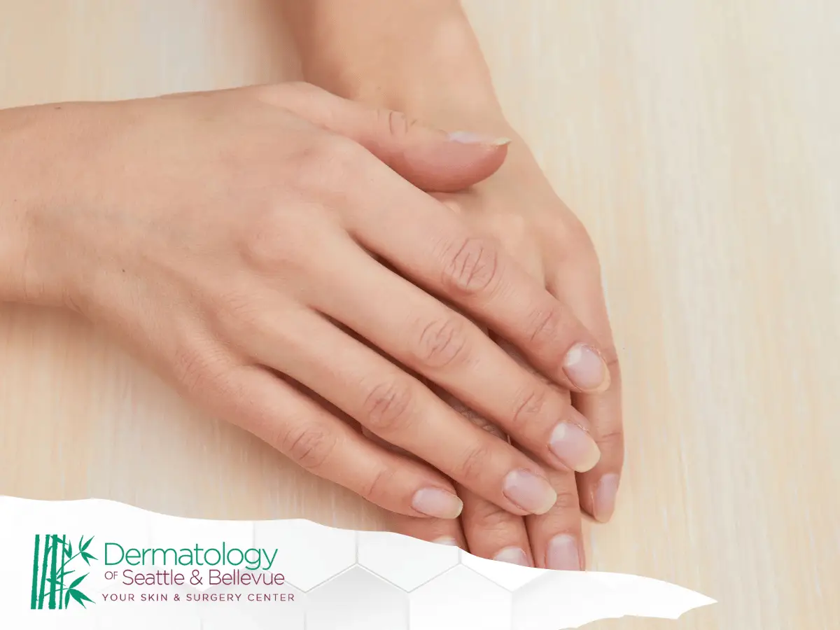 Close-up of crossed hands resting on light wooden surface.