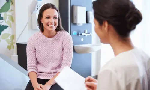 Smiling woman in pink sweater talks with healthcare professional in clinic