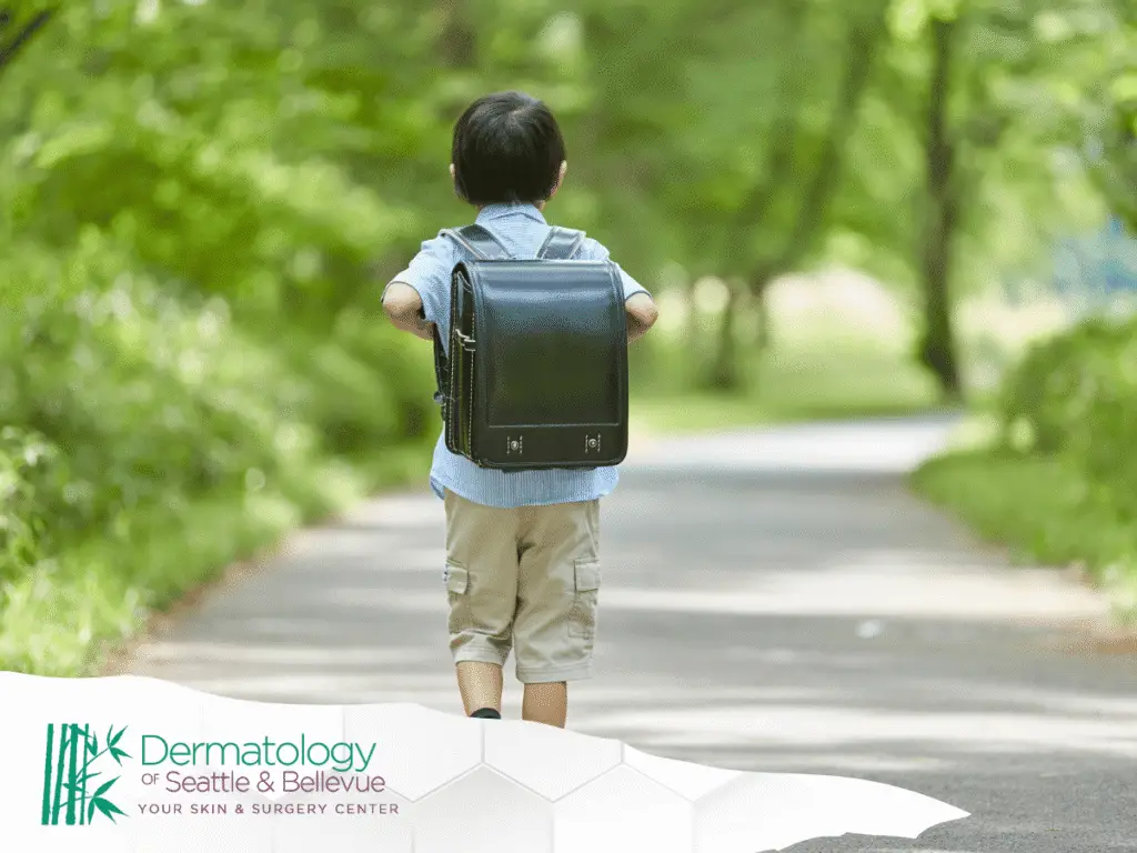 Young child with backpack walking alone on a tree-lined path.