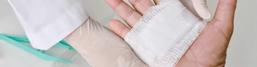 Gloved medical worker bandaging a person’s open palm with gauze