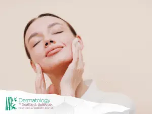 Woman with closed eyes gently touching her face, neutral background.