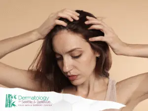 Woman touching her scalp with both hands, looking downward thoughtfully.
