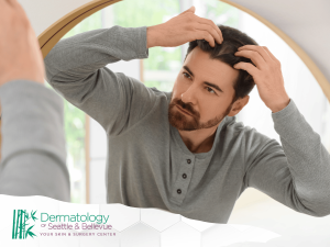 Man examining his hair in a bathroom mirror, wearing a gray long-sleeve shirt.