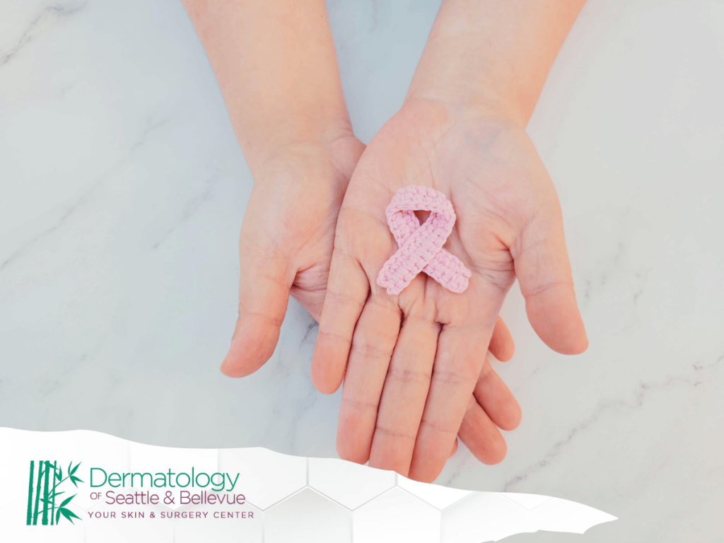 Two hands holding a pink ribbon on a marble background.