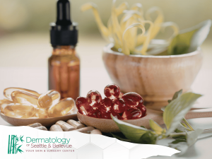 Clear capsules, red gel capsules, and a dropper bottle on a wooden table with green leaves.