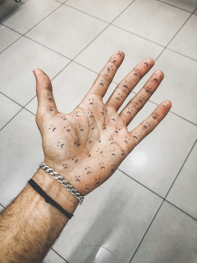 Palm of a hand with multiple small sad face tattoos on a tiled surface.