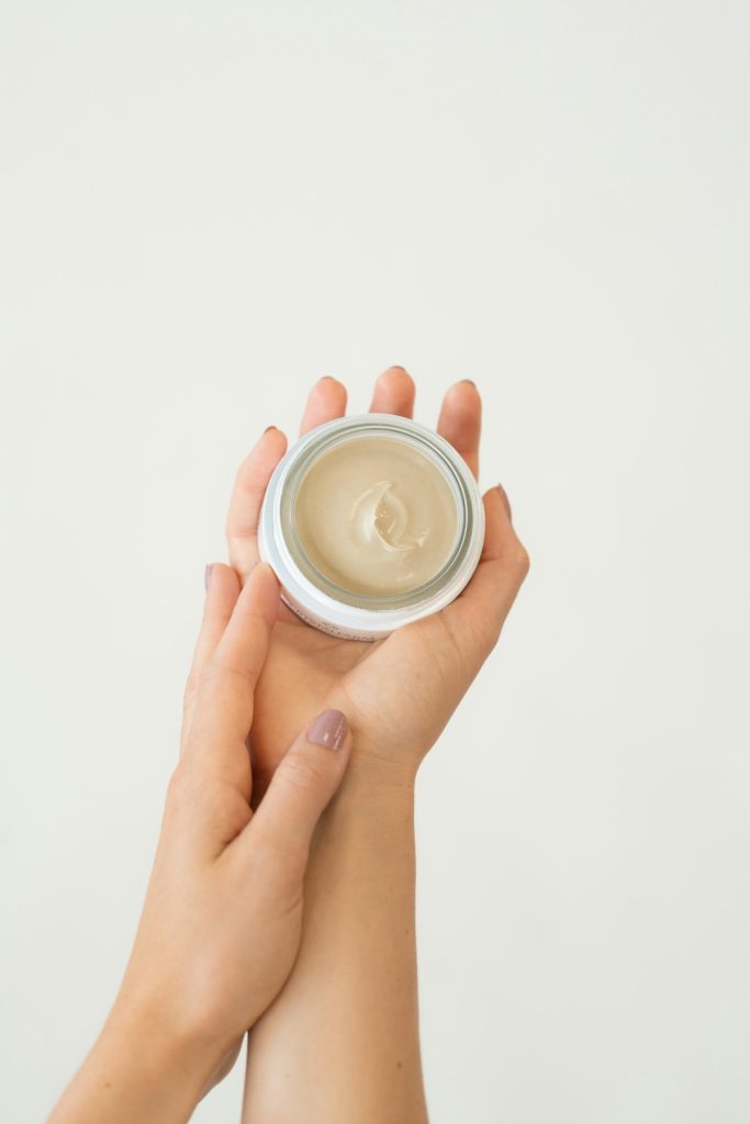 Hands holding a small jar of cream with a light beige substance inside.