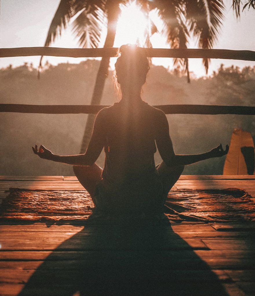 Silhouette of a woman meditating at sunset, surrounded by palm trees.