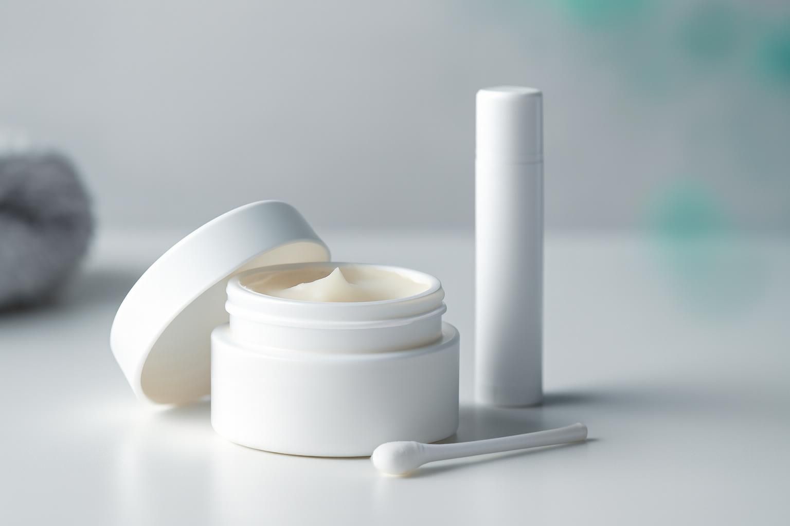 Open white skincare cream container with a small applicator beside it.