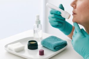 Woman in teal gloves using a skincare device near a tray of supplies.